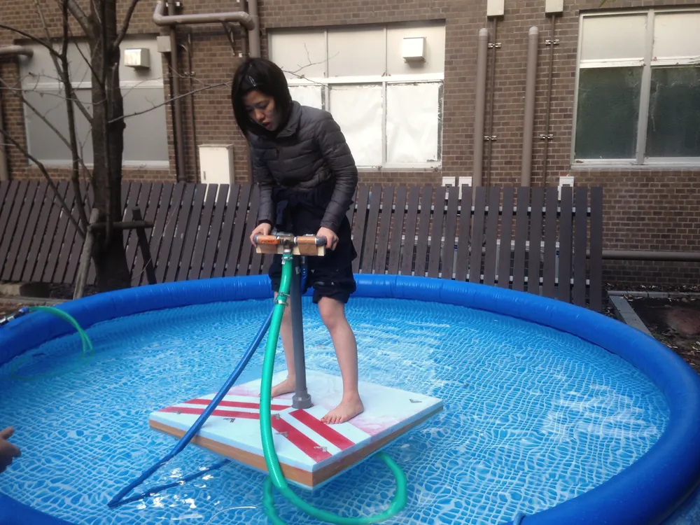 A student stands on a hand-built board prototype floating in an inflatable pool to test it