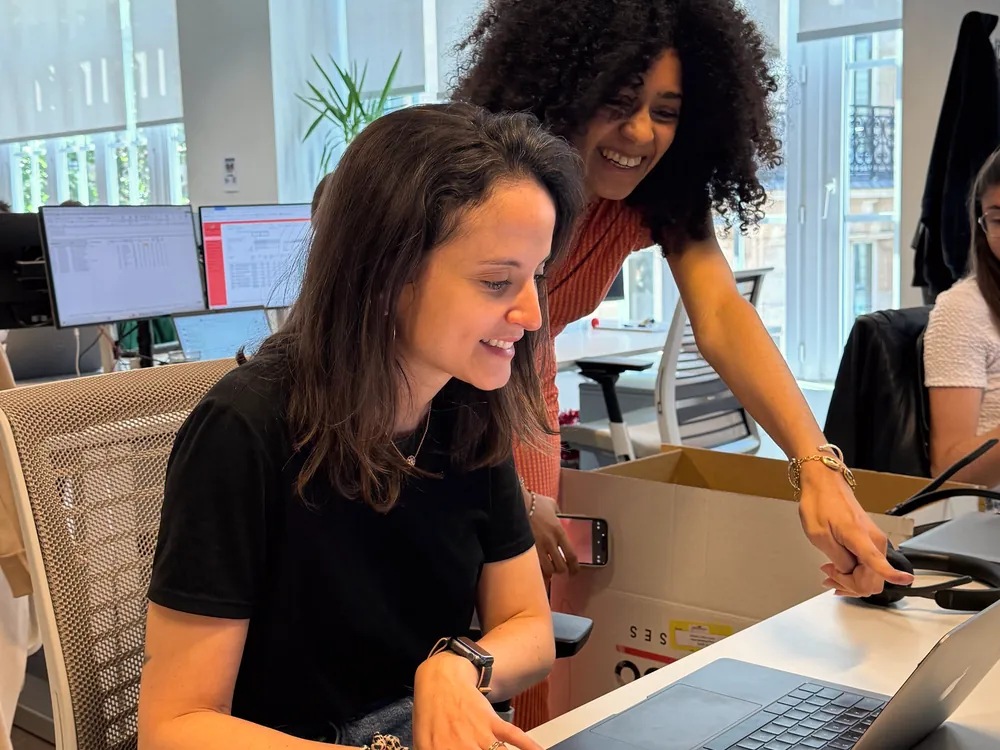 Two women smile while testing a software prototype on a laptop at an office desk
