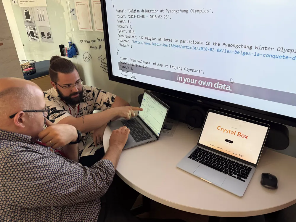 Two people test a software prototype on laptops at a table in front of a large screen
