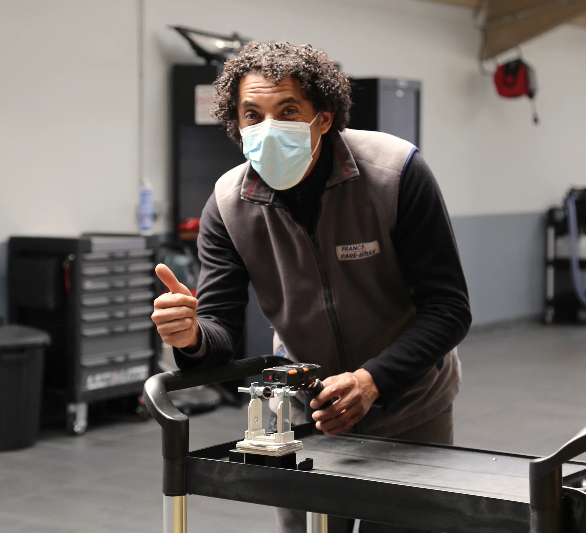 A technician in a face mask gives a thumbs-up while testing a prototype on a workshop trolley