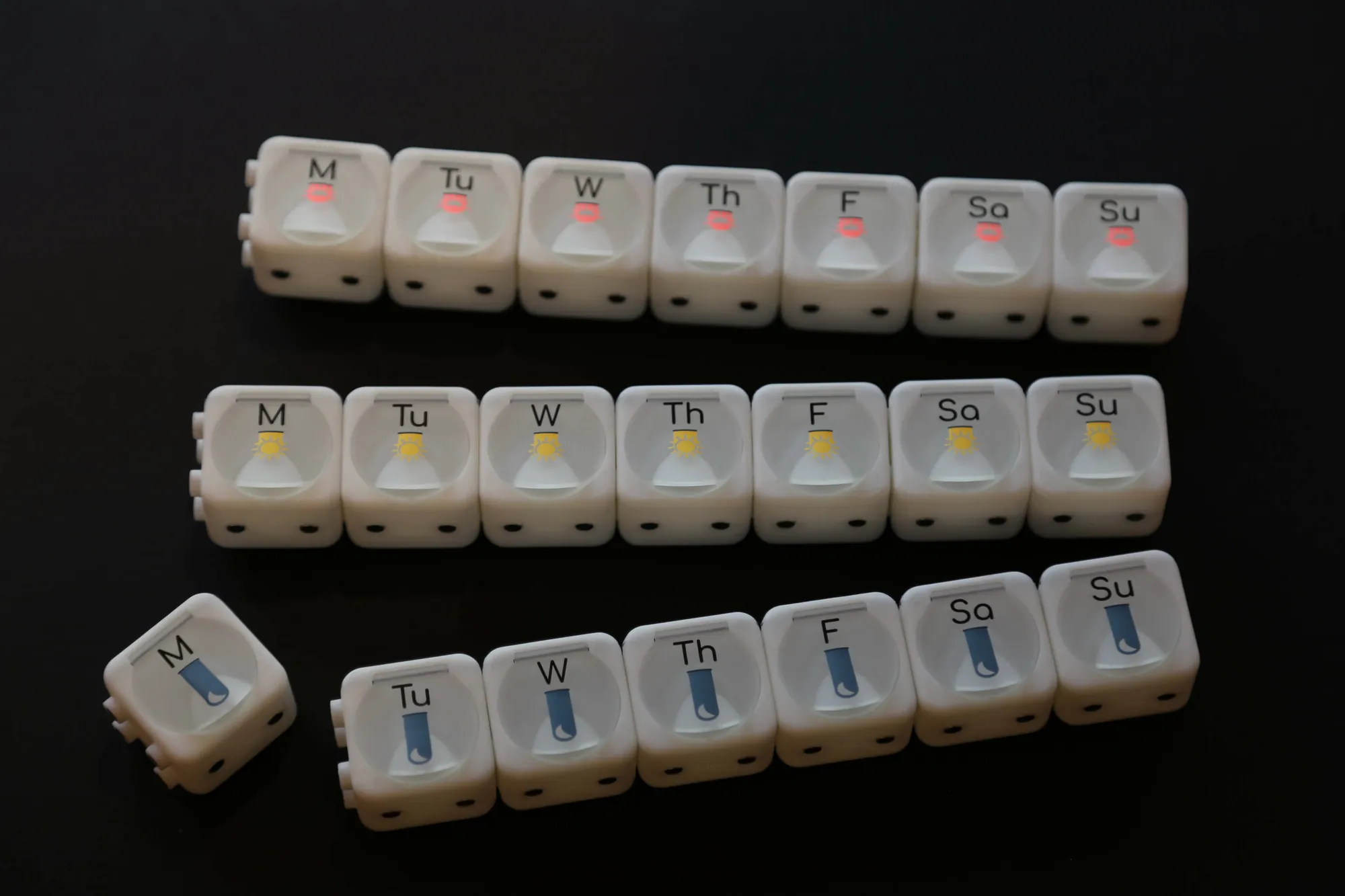 A pill-box prototype with one compartment per weekday on a black background