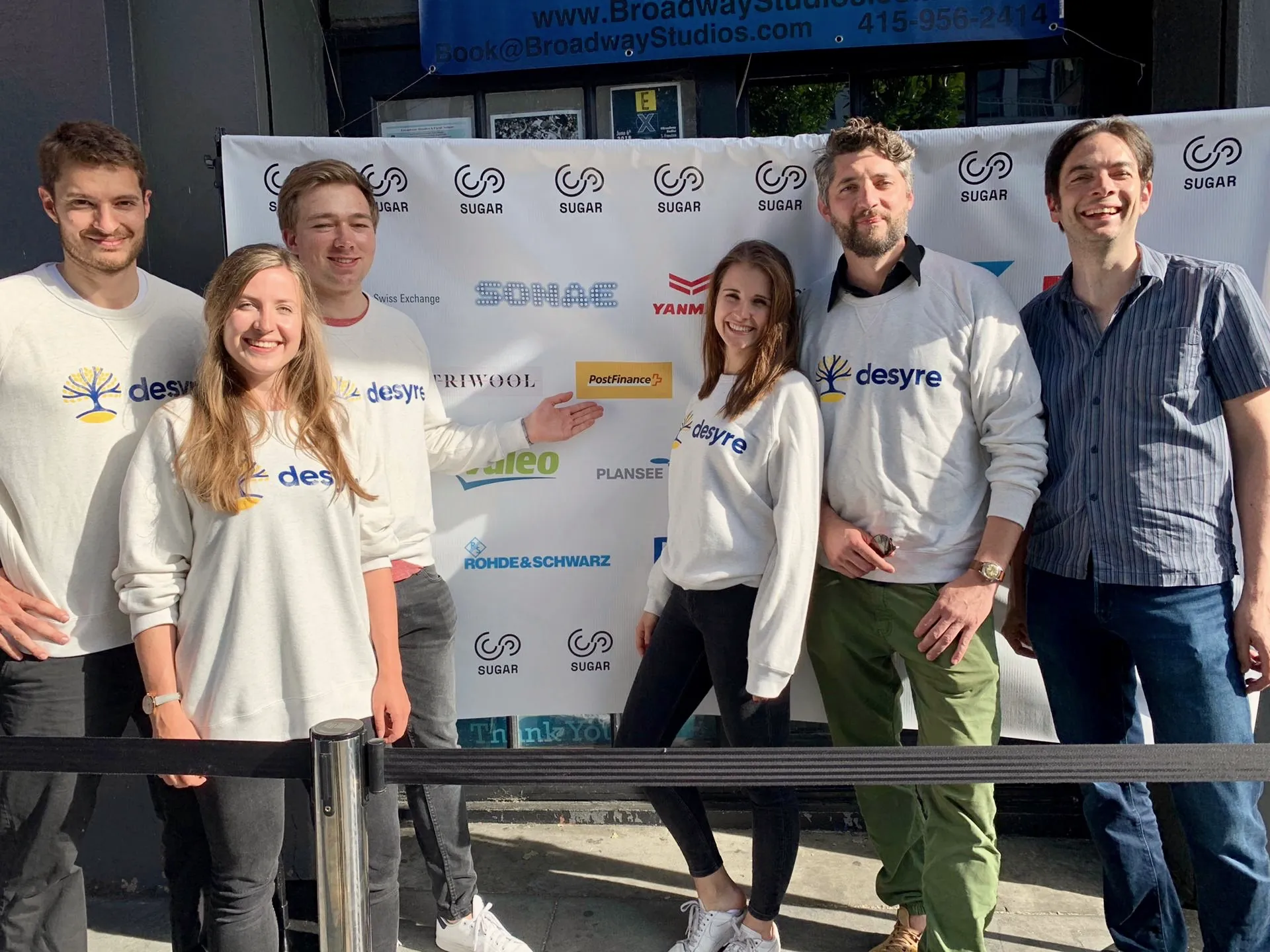 A project team in matching sweatshirts poses in front of the sponsor wall at the SUGAR Expo 2019 in San Francisco
