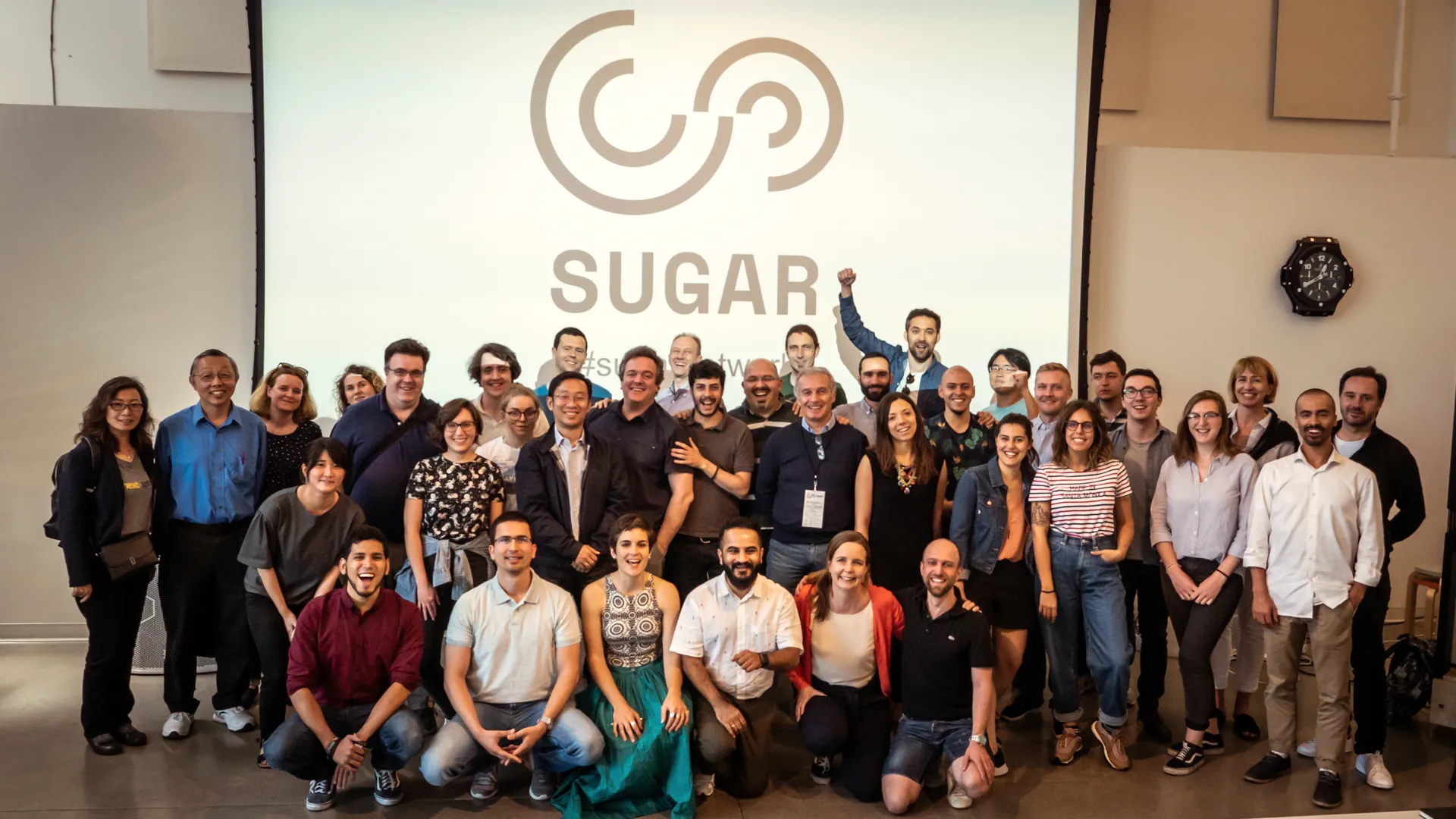 A large group of the SUGAR community poses under the SUGAR logo at the Expo 2019