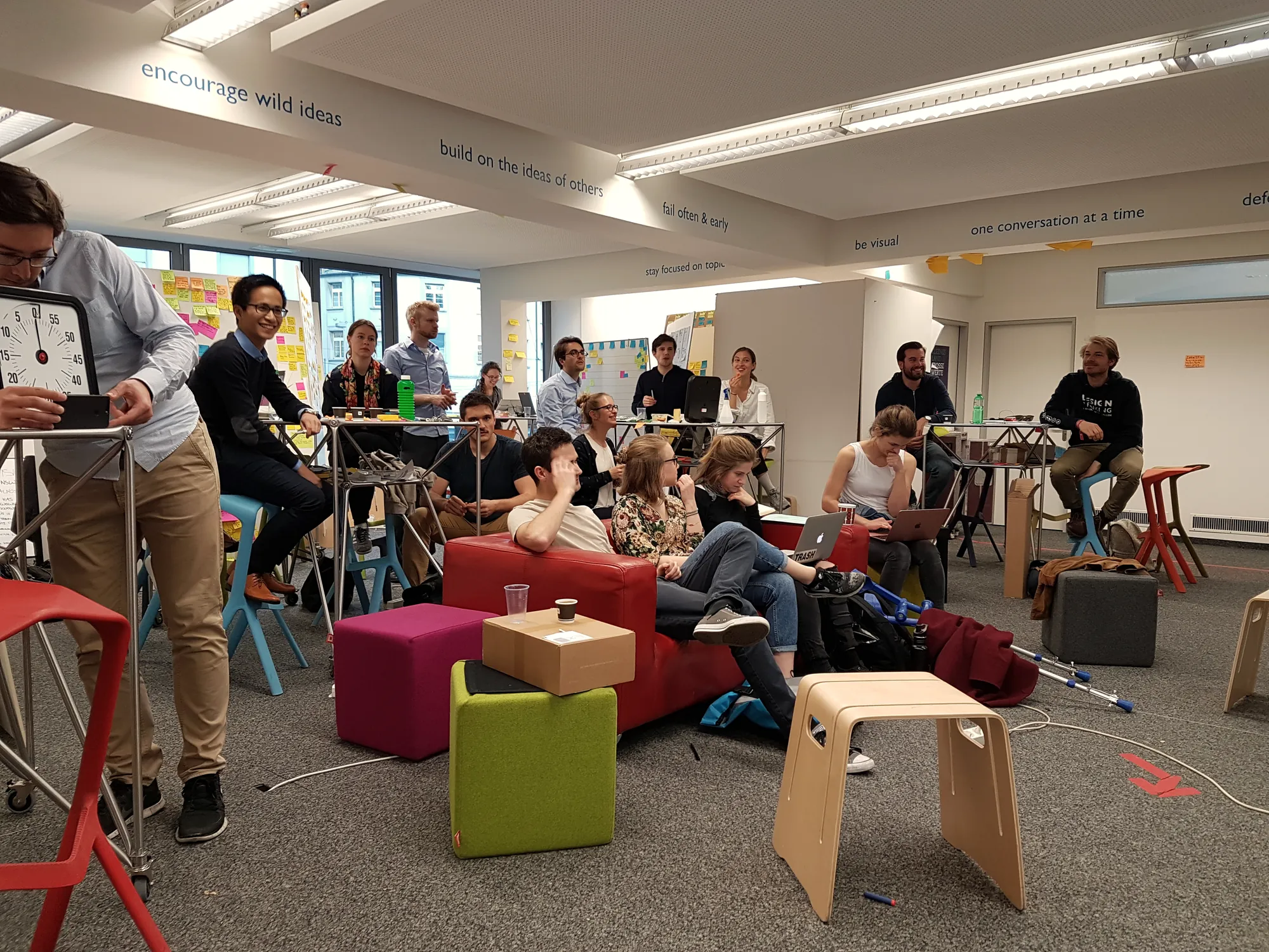 Teams at work on sofas and stools in a busy workshop space with post-it walls