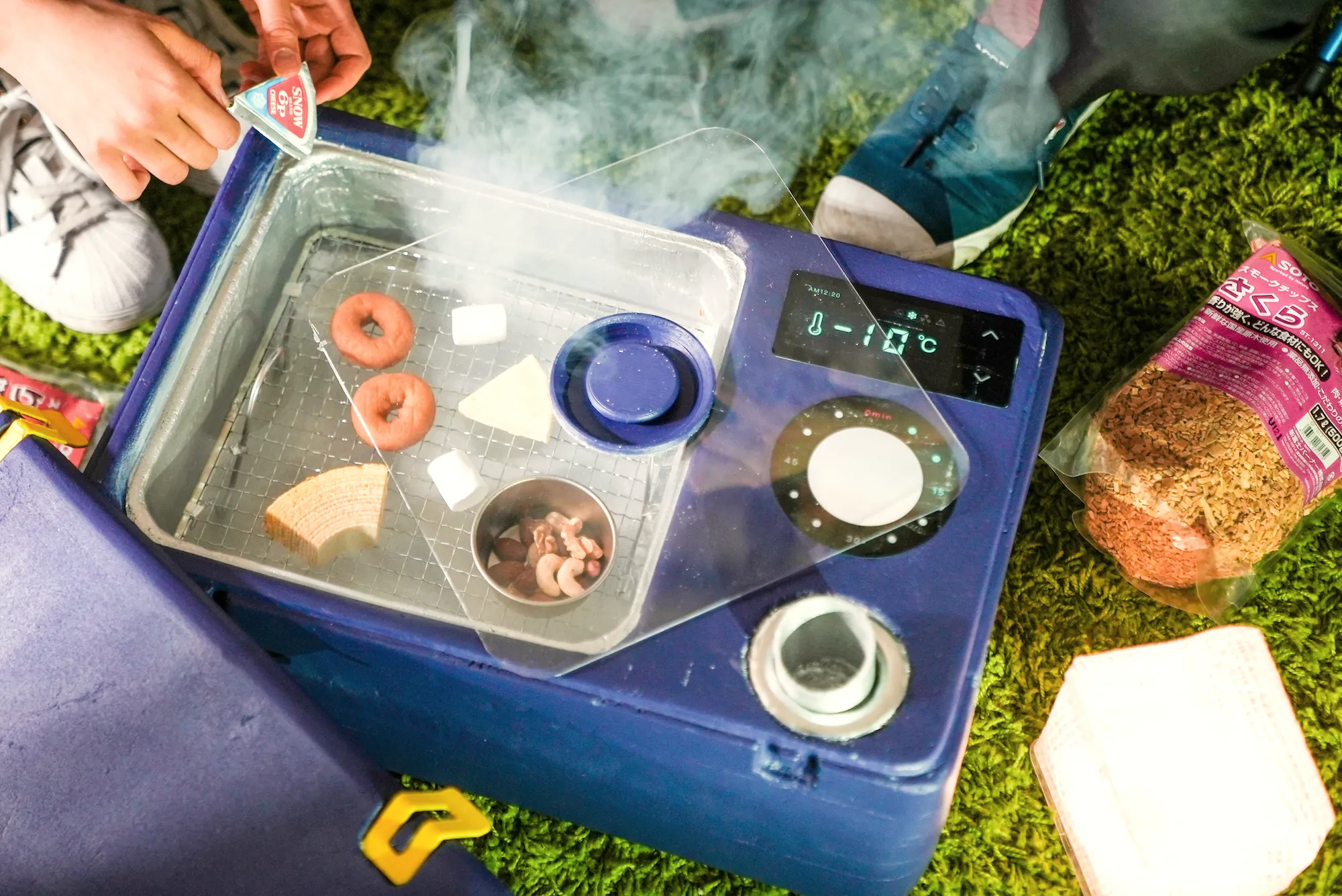 A cooler-box prototype with food on grass, steam rising from a cooling compartment